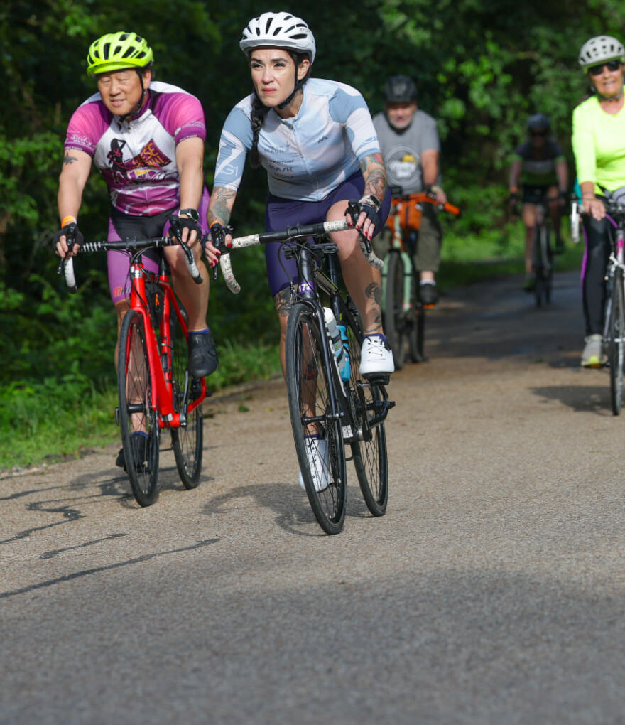 Dani riding at the front of a group ride on a tree-lined road, Bryan beside her.